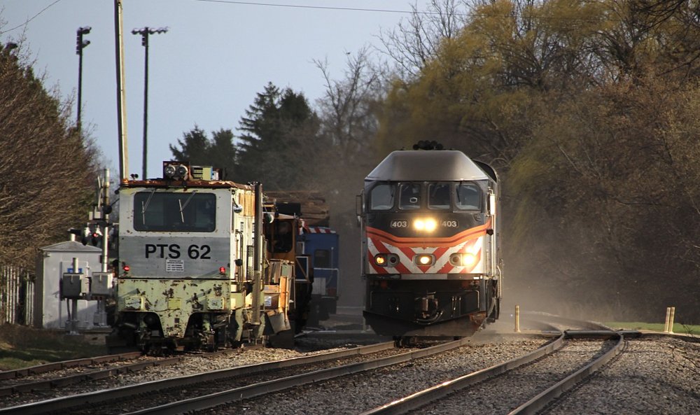 Commuter train passes green maintenance of way machinery