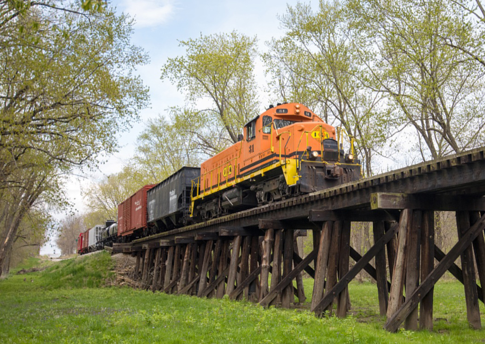 Orange locomotive pulling seven cars crosses wooden bridge