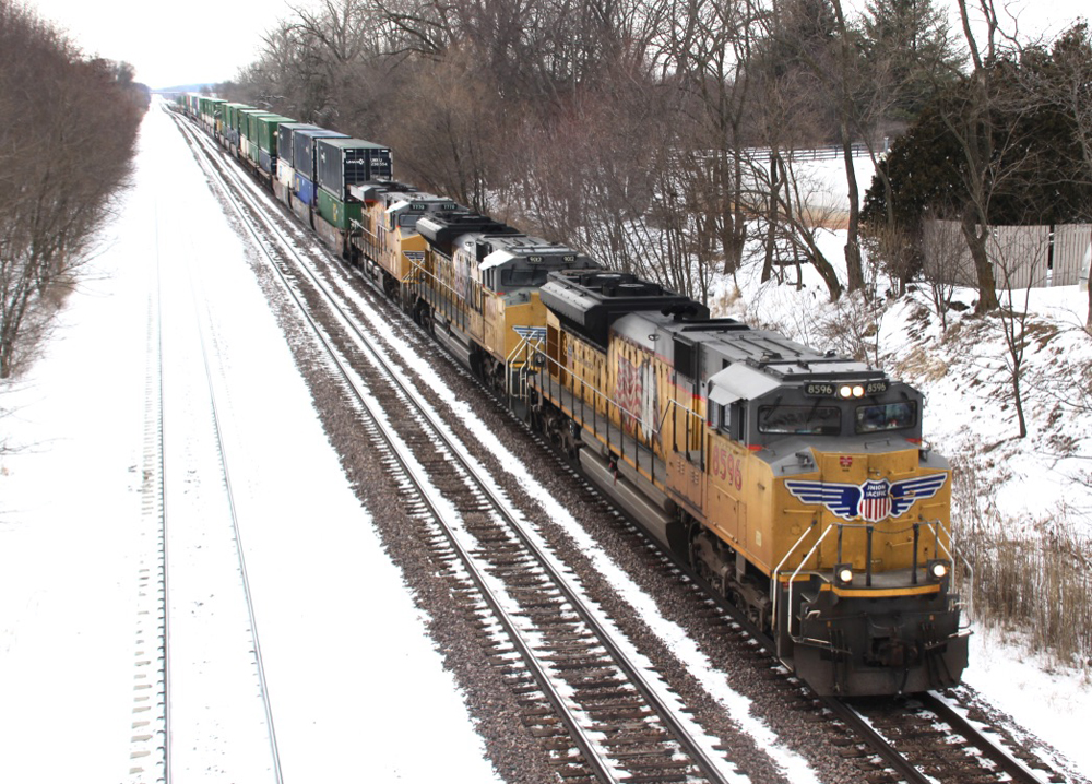 Yellow locomotives lead container train in snowy landscape