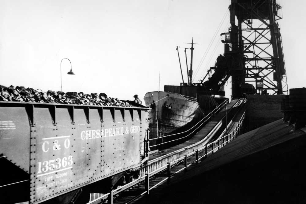 Coal hopper moves along unloading trestle alongside ship