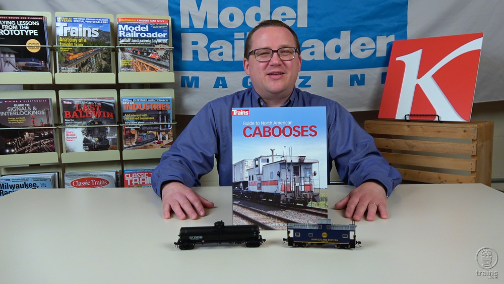 Cody Grivno holds Guide to North American Cabooses book, with a black HO scale single dome tank car and dark blue Norfolk and Western caboose in front of him