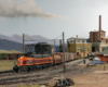 A maroon-and-orange double-ended electric locomotive couples onto a manifest train in front of a depot