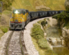 A yellow-and-gray Union Pacific SD7 diesel runs downgrade with a coal train along a racing creek