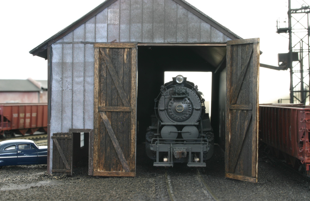 The nose of a steam locomotive is seen through the door of a single-stall wooden engine house