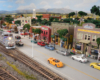 A pair of modern diesels rolls a freight train past a bustling downtown scene