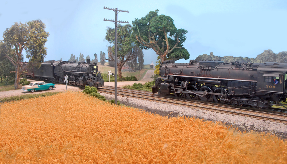 Two HO scale Nickel Plate Road steam locomotives meet at a rural grade crossing on Tony Koester’s HO scale model railroad.