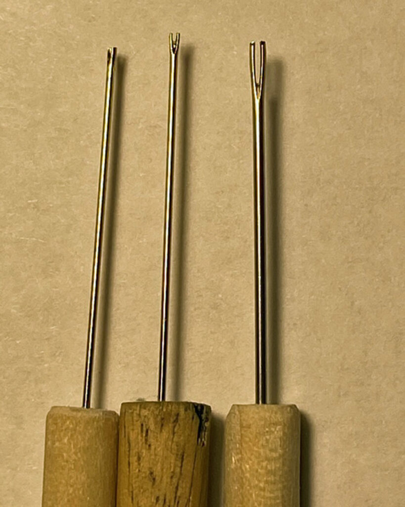 Three sewing needles with their eyes snipped across, inserted in dowel handles