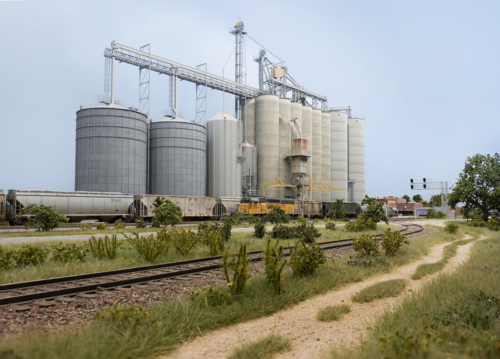 The concrete and corrugated metal silos of a large grain complex dwarf passing trains