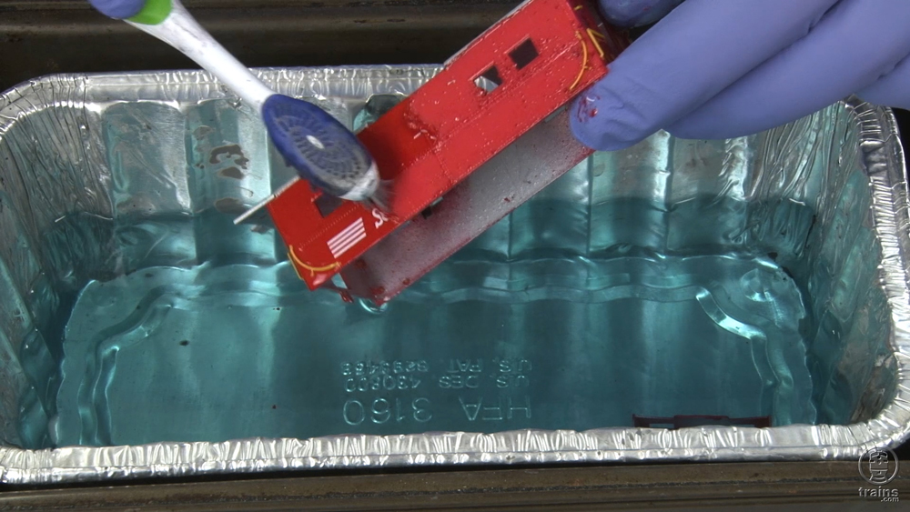 Piece of a train car being dipped in chemicals and scrubbed with a toothbrush