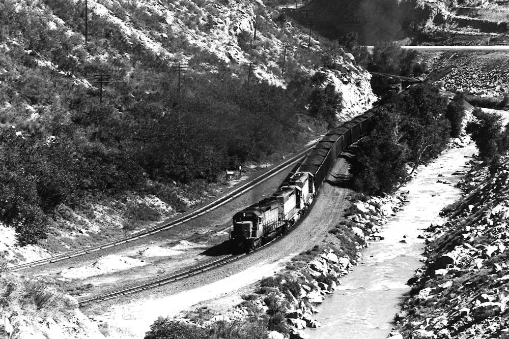 Diesel locomotives with coal train along river in canyon