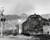 Dirty diesel locomotive leads a freight train through a road crossing