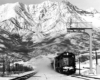 Freight train kicking up snow under a signal gantry