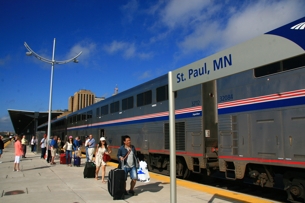 People walk on platform in front of bilevel passenger cars