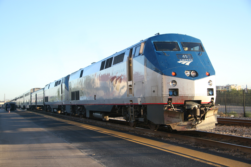 Two silver locomotives with passenger train at station