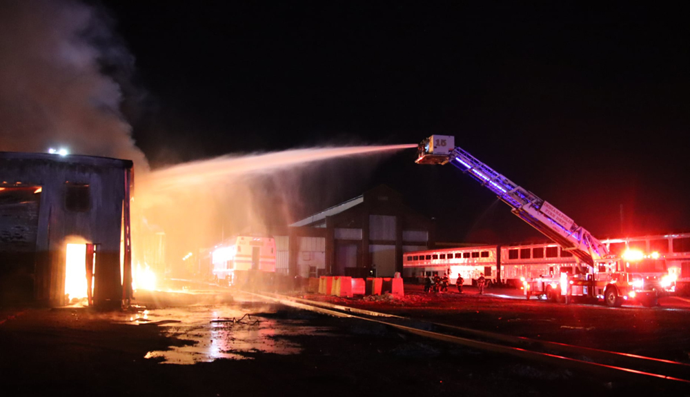 Fire truck spraying water on burning building with passenger cars in background