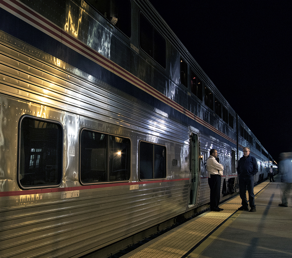 Two men speaking on a station platform in front of a passenger car.