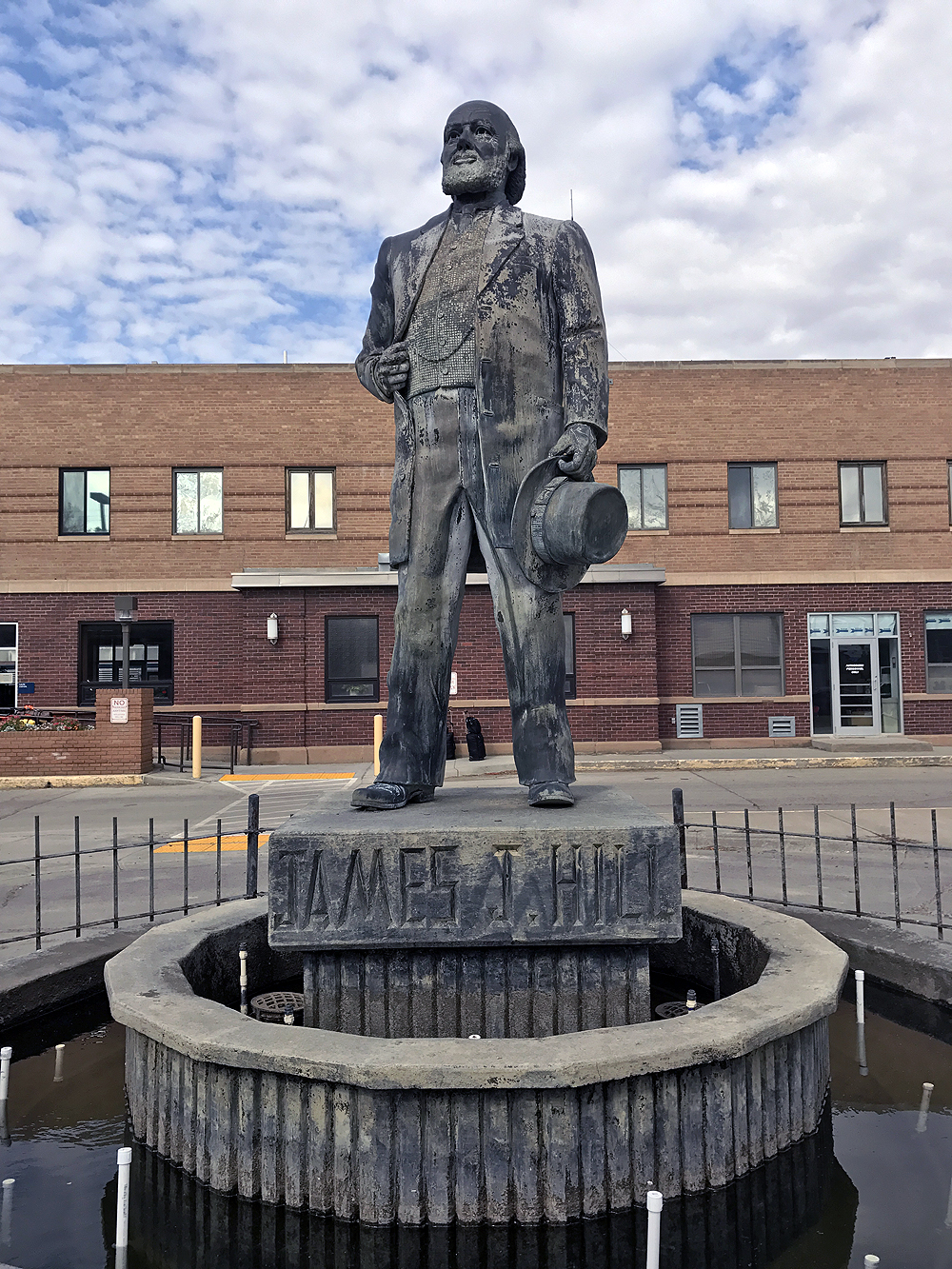 Statue inside concentric stone and iron fence circles with a brick building in the background.