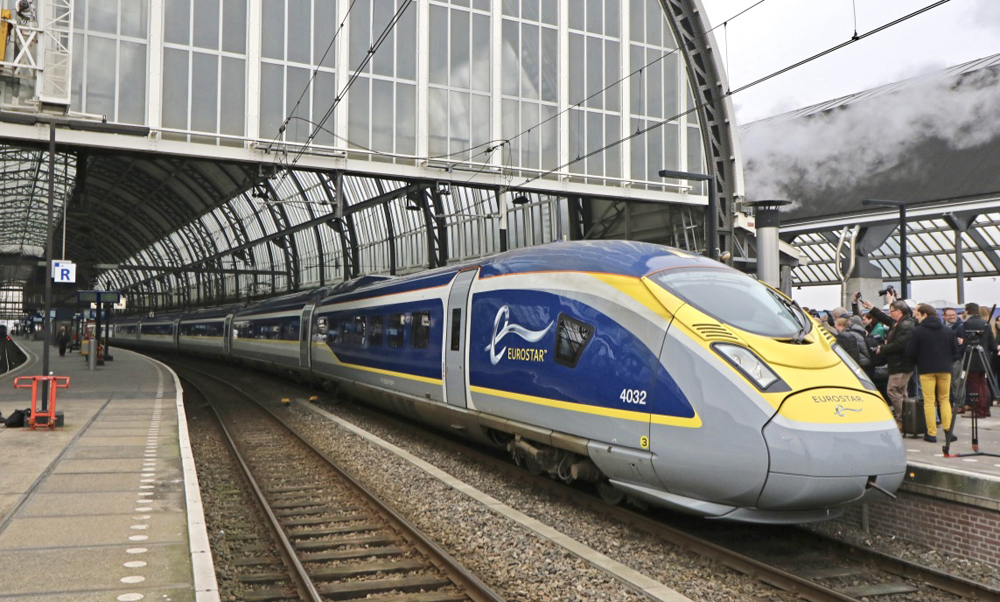 Blue, gray, and yellow high speed train in station, partially under trainshed