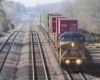 Yellow locomotive pulling stacked container cars on undulating straight track. 