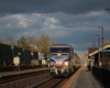 Train with blue and silver locomotive at station platform under billowing clouds.