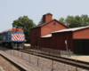 Train passes red wooden barn.