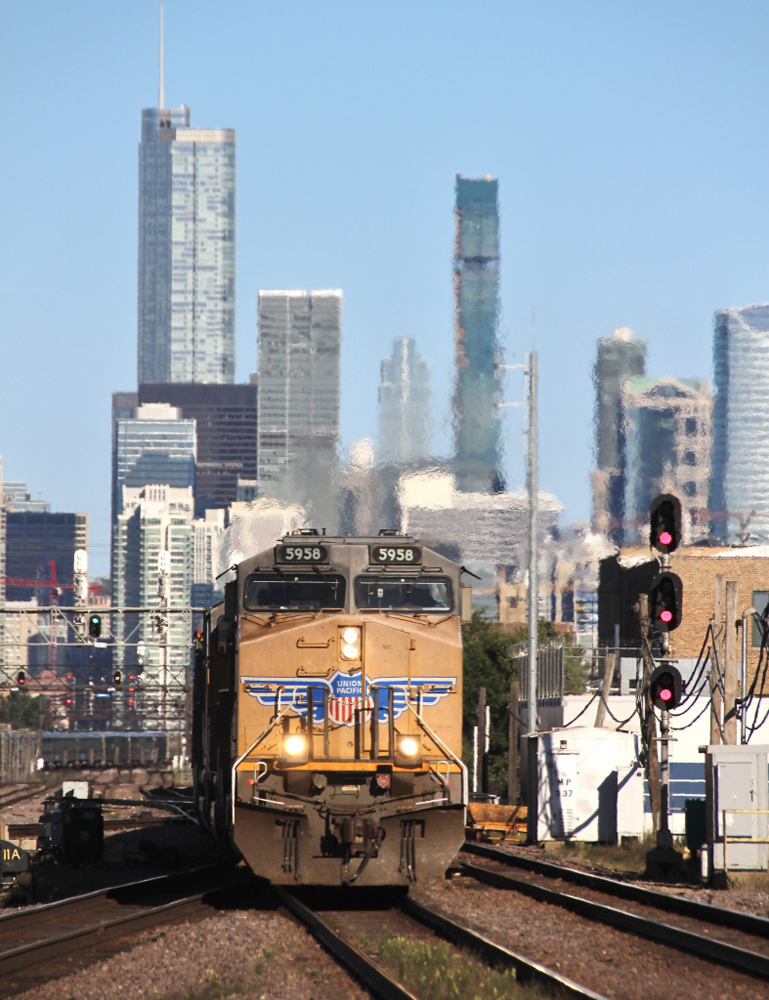 Yellow locomotive leads train with city skyline in background