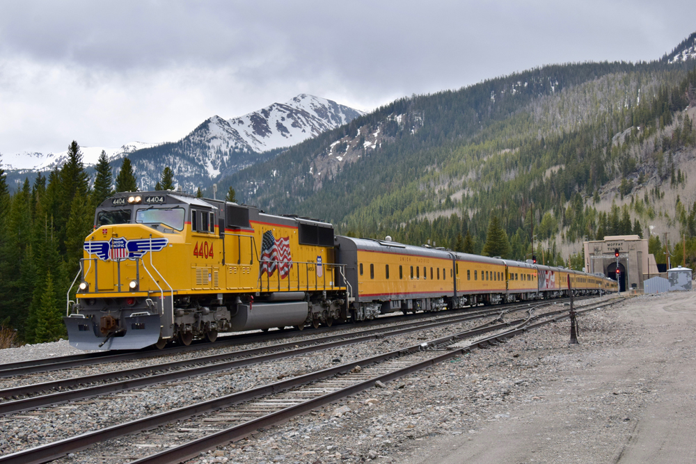 Yellow locomotive and passenger cars at tunnel.