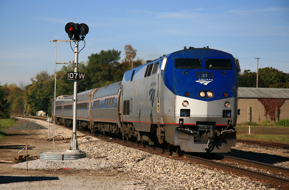 Short passenger train with blue and silver locomotive passes signal