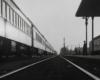 A train next to a station where a man stands smoking