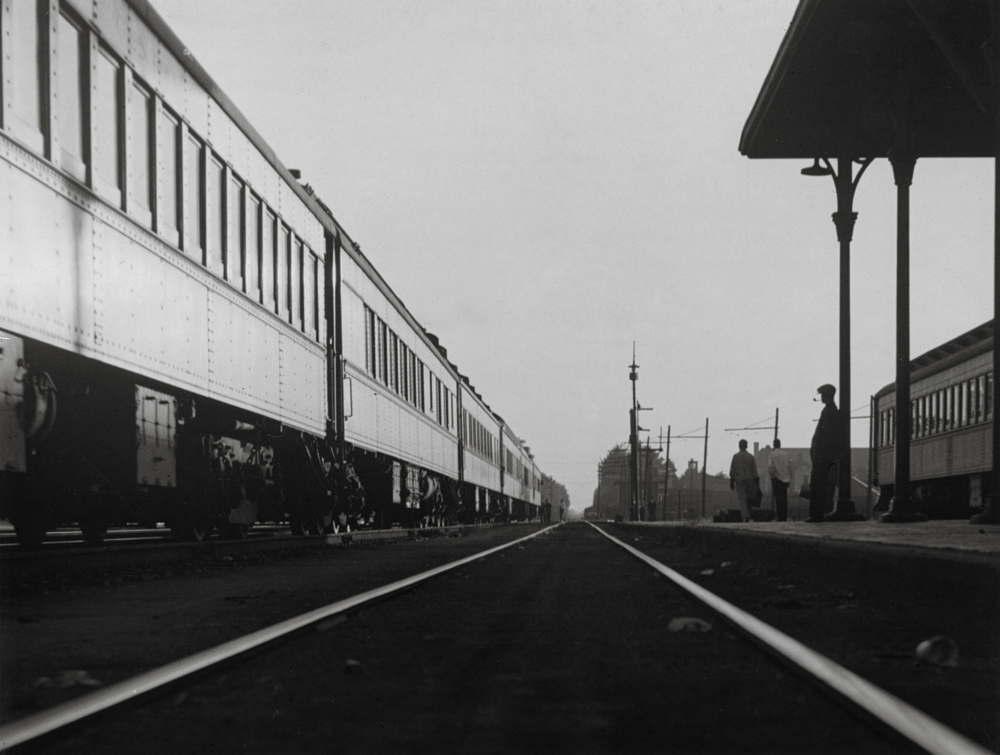 A train next to a station where a man stands smoking