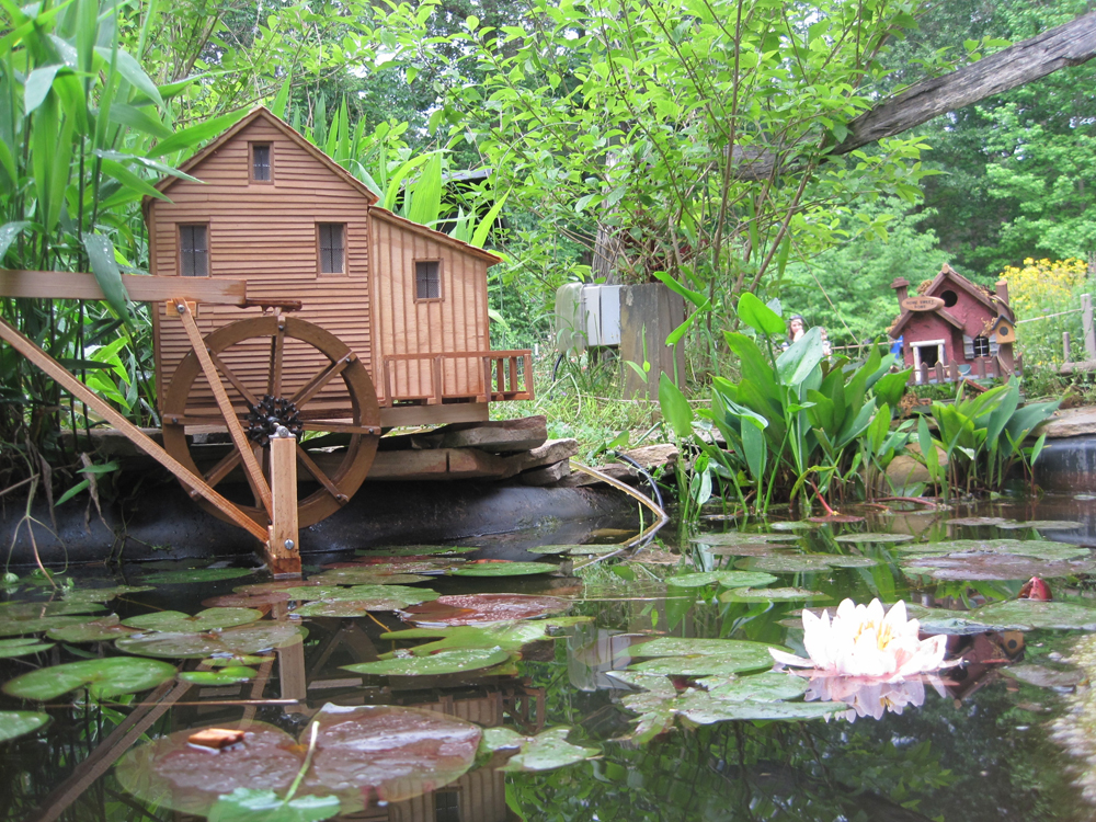 A model mill with water wheel near a small pond.