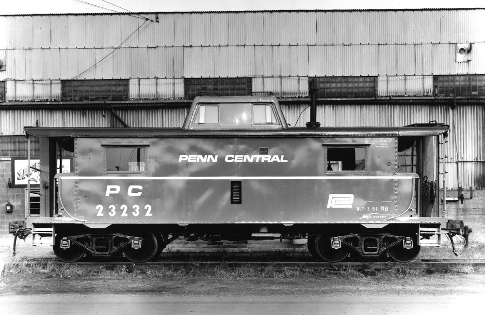 A black-and-white photo of a Penn Central caboose with a white side stripe