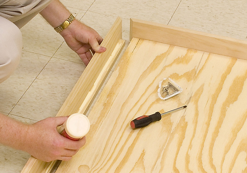 Steven Otte applies glue to a board as he assembles benchwork on the workshop floor