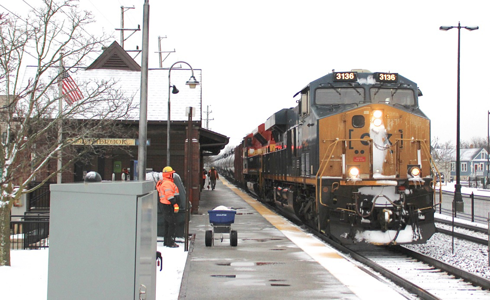 Unit oil train passes passenger station with ground covered with snow