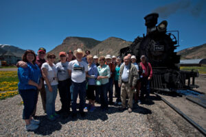 A Trains tour group poses next to a narrow gauge steam locomotive in Silverton, Colorado.