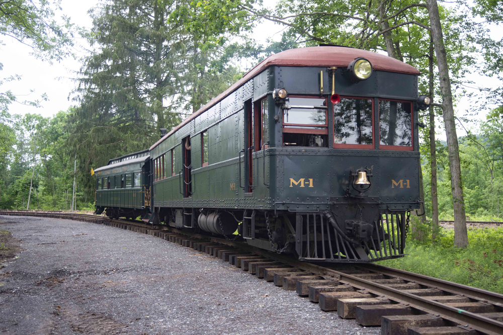 Dark-green gas-electric car pulling passenger car