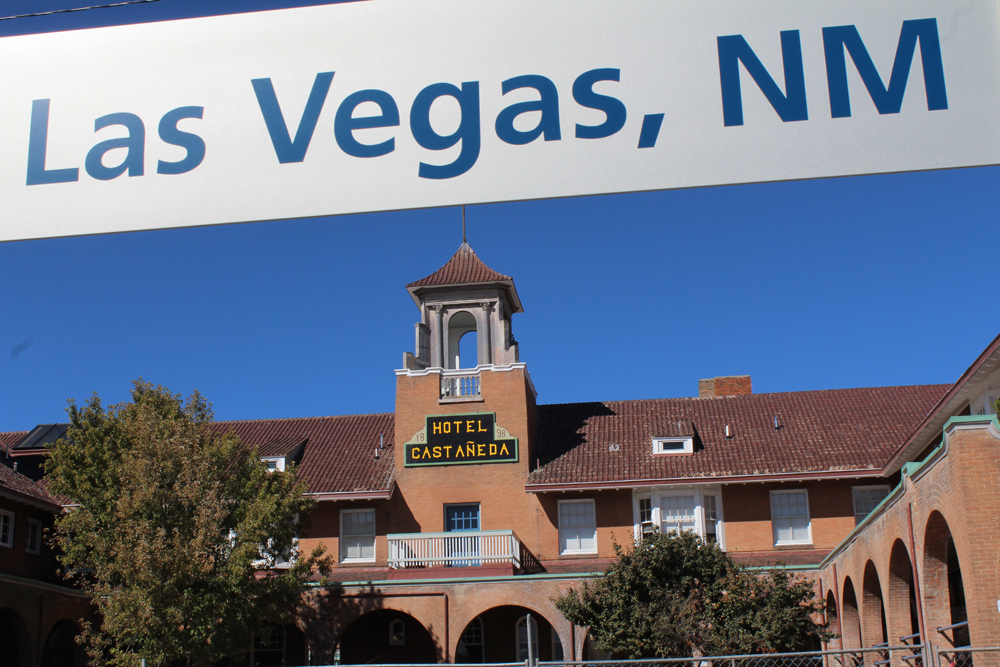 Las Vegas, N.M., station sign with Spanish-style hotel in background