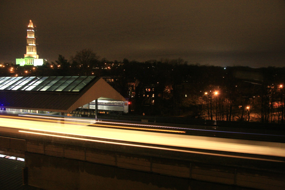 One train stopped at station at night while another passes in a blur of light