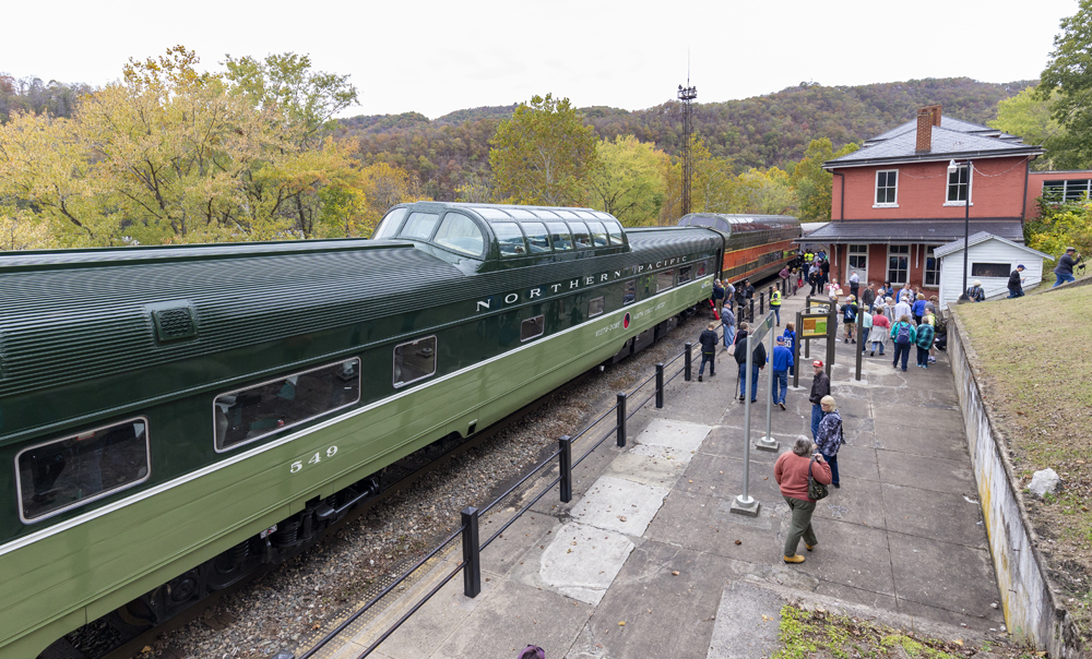 Two-tone green dome passenger car in a wood scene at a station.