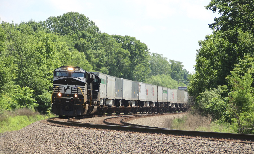 Black locomotives followed by cars carrying truck trailers
