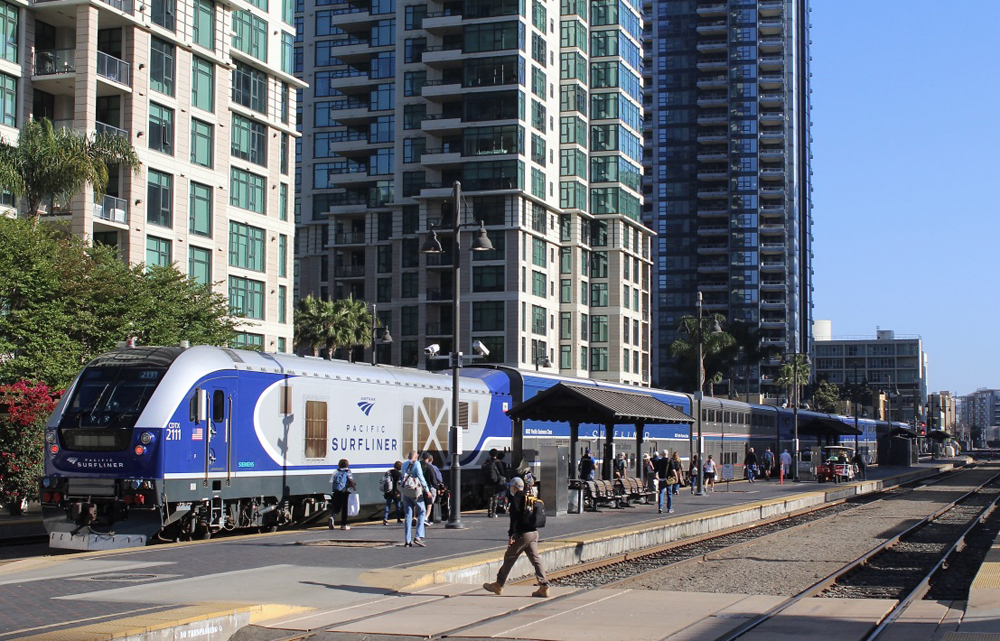 Blue and silver locomotive and passenger train at platform in front of skyscrapers