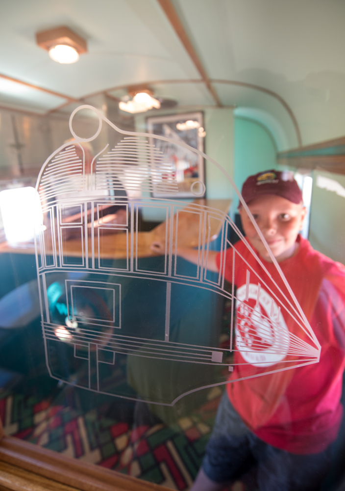 Boy in red shirt looks through glass etched with image of train