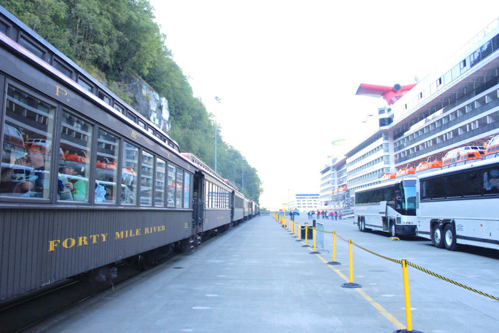 Train with wooden passenger cars waits on dock across from cruise ship