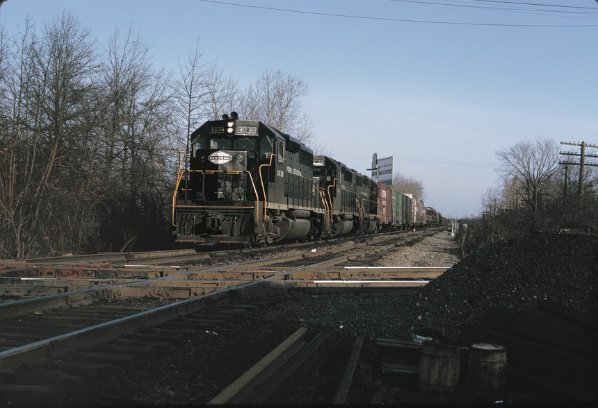 Black diesel locomotives haul freight train toward diamond crossing