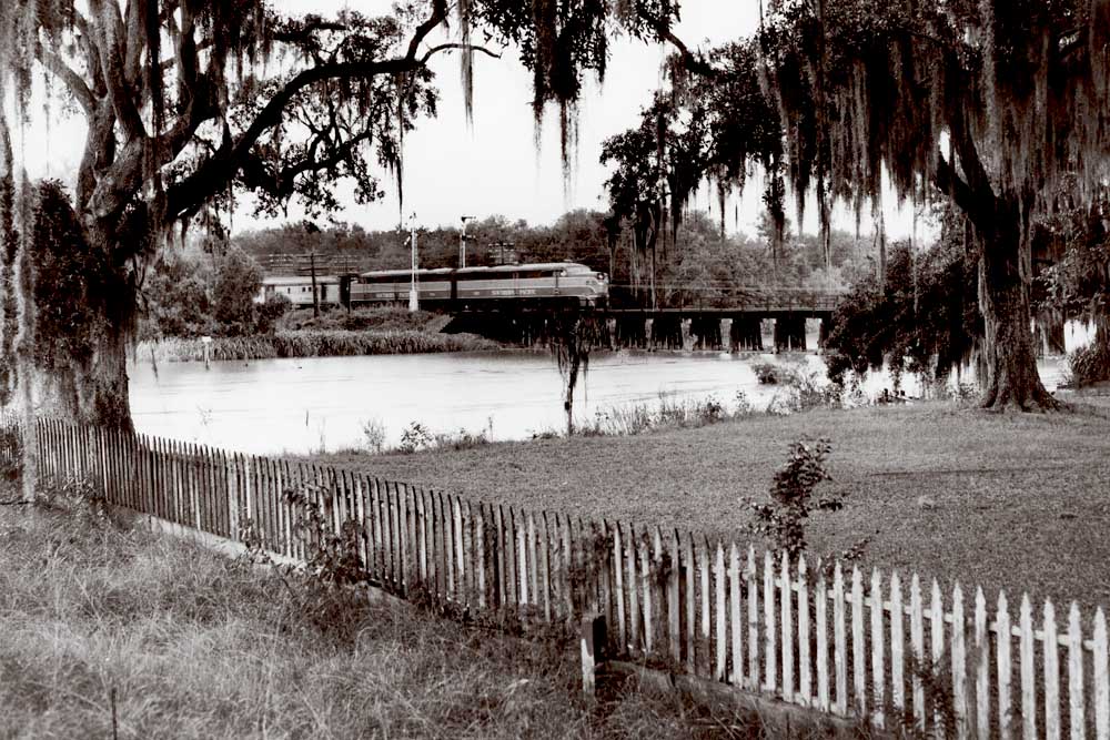 Passenger train on wood trestle with semaphore signals framed by moss-covered trees