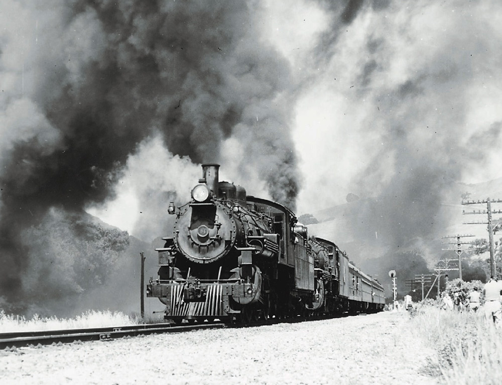 Doubleheaded steam locomotives making smoke during a photo run-by for railfans.