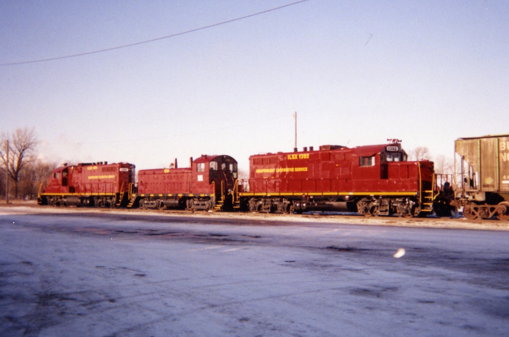 Two four-axle road locomotives frame an end-cab switcher in a snow-covered railroad yard.