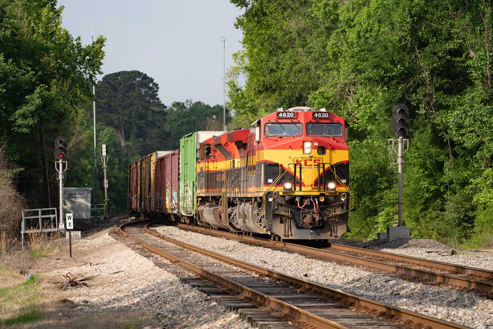 Red, yellow, and black diesel locomotives bring a freight train around a curve and between signals