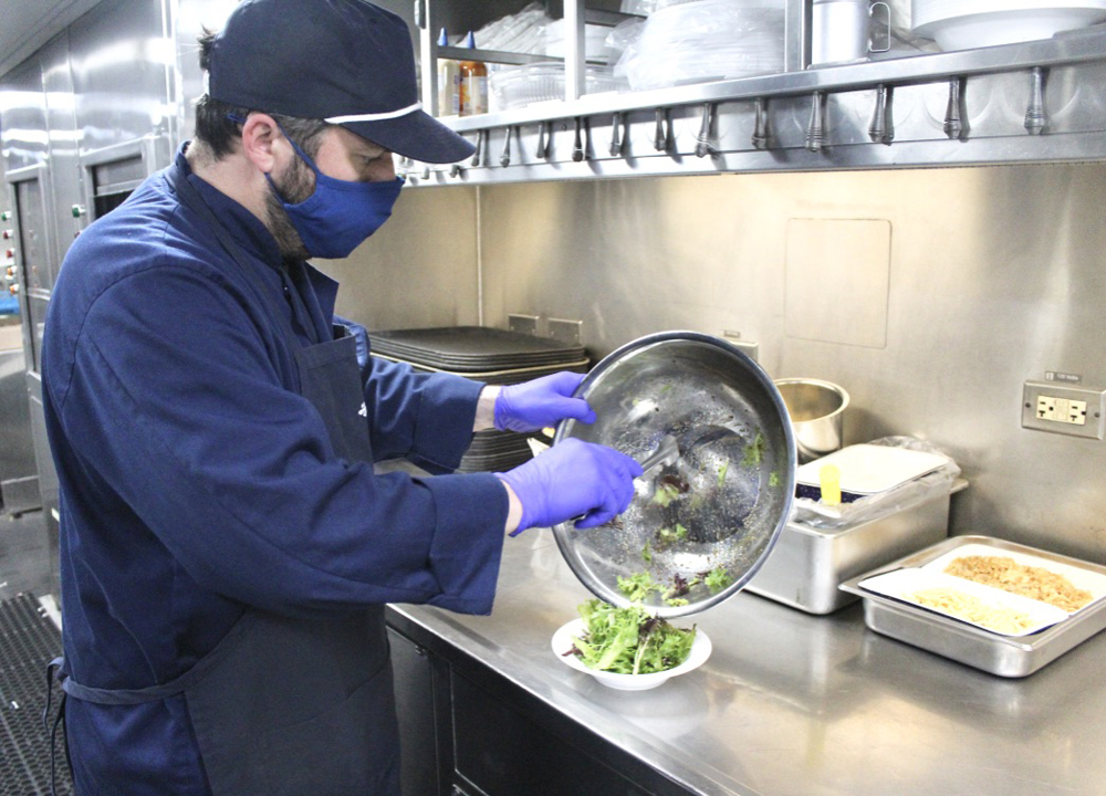 Man moving salad from mixing bowl to dish