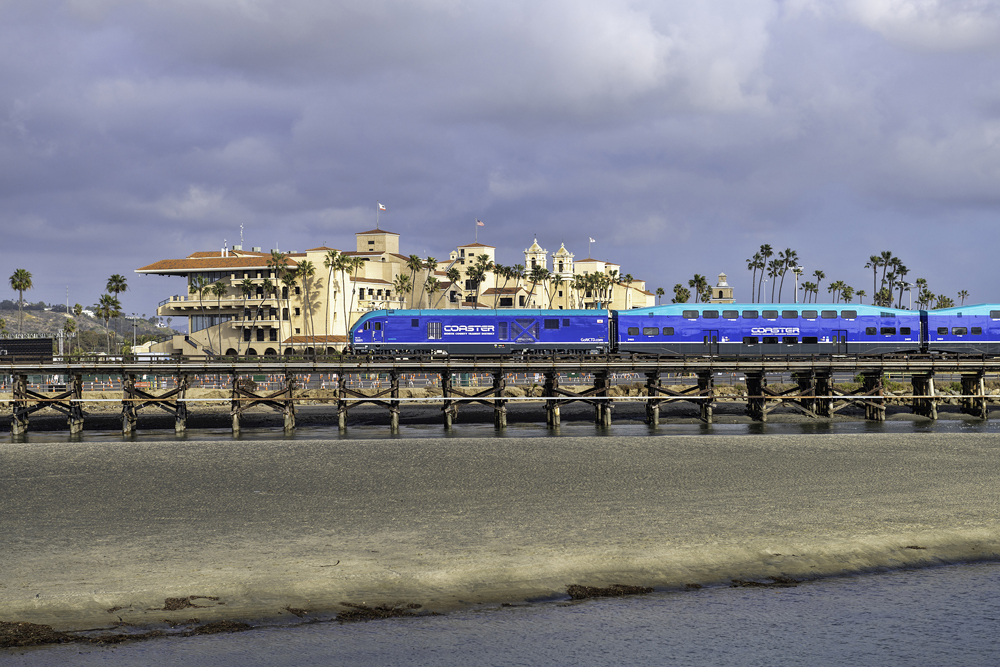 Commuter train with blue paint scheme passes large grandstand structure